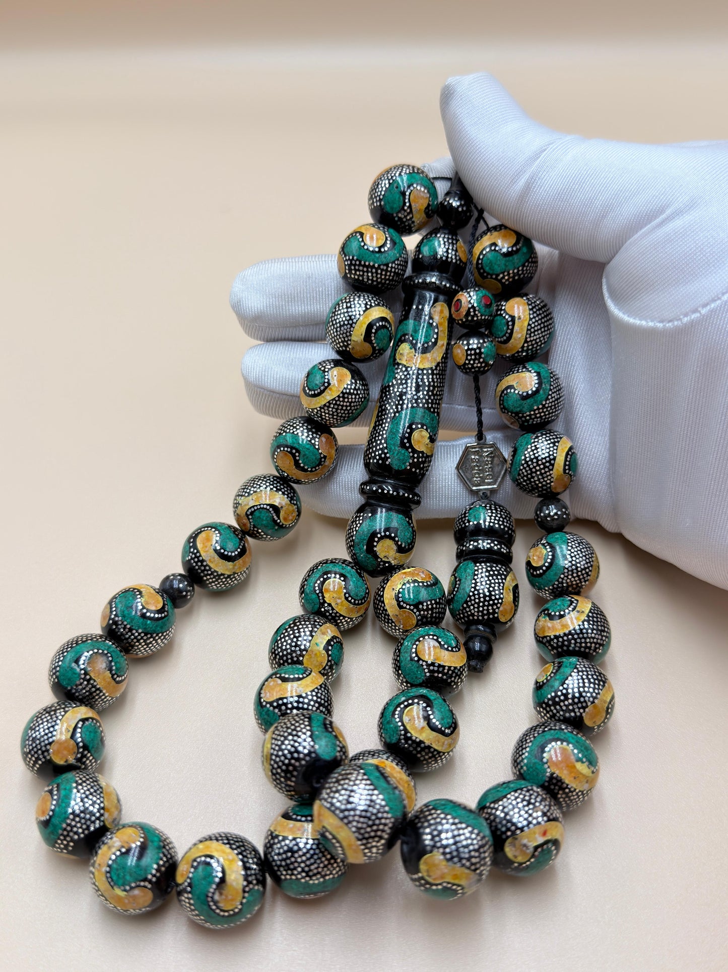 يسر بحر أحمر، مطعّم بالفضّة الخالصة عيار 925، ومزيّن بـ الكهرمان الطبيعي والملاكيت.
Red Sea Yusr, inlaid with 925 sterling silver, adorned with natural amber and malachite.