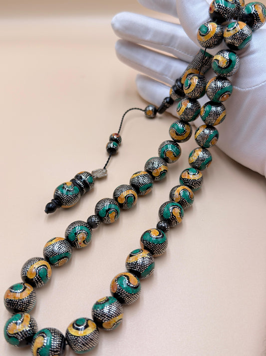 يسر بحر أحمر، مطعّم بالفضّة الخالصة عيار 925، ومزيّن بـ الكهرمان الطبيعي والملاكيت.
Red Sea Yusr, inlaid with 925 sterling silver, adorned with natural amber and malachite.