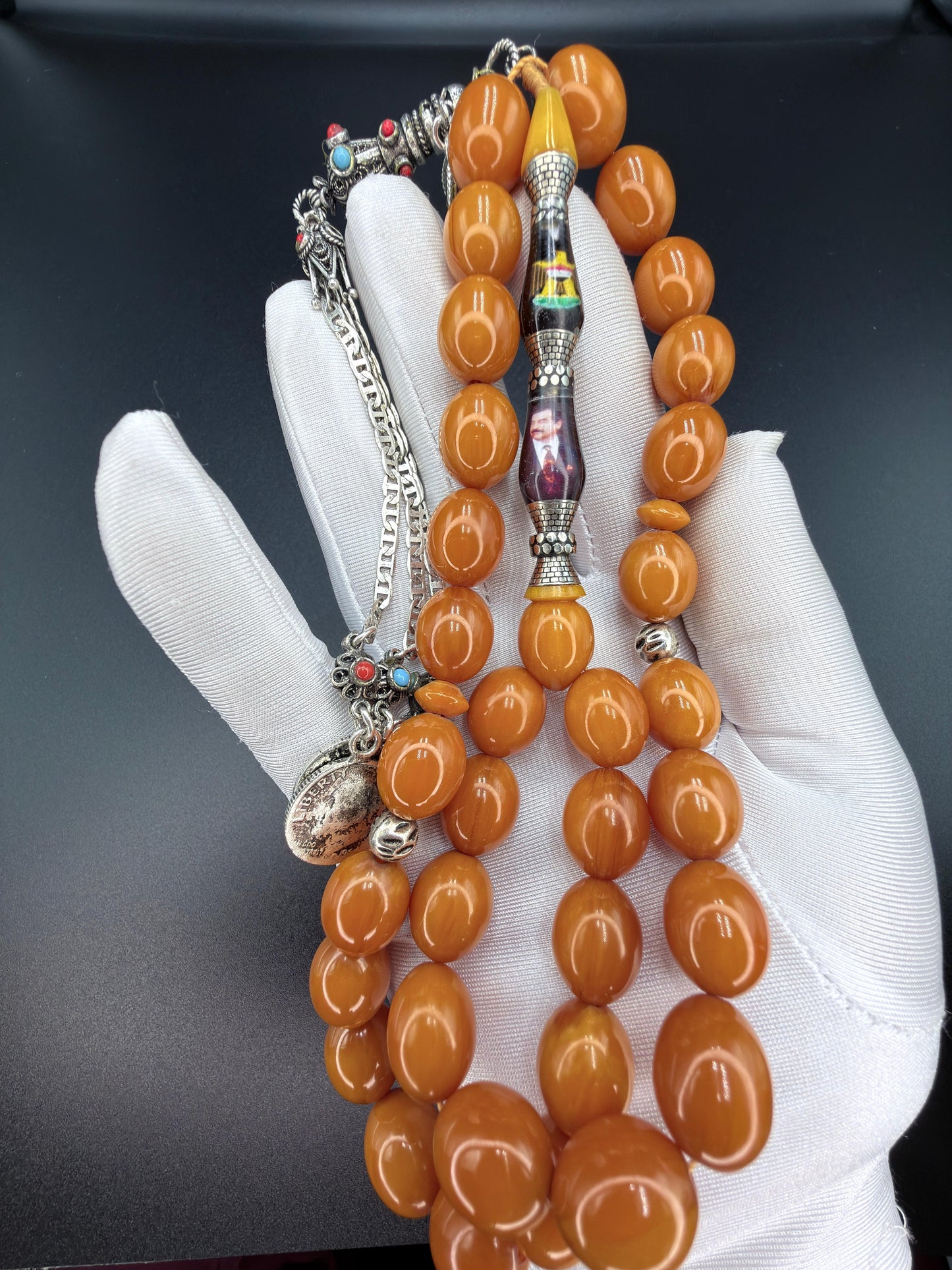 Unique musk Misbaha featuring the image of Saddam Hussein and the Iraqi national anthem, paired with a 500-grade silver tassel. مسباح مسكي مميّز يحمل صورة صدام حسين والسلام الجمهوري، مرفق بشرّابة فضّة عيار 500