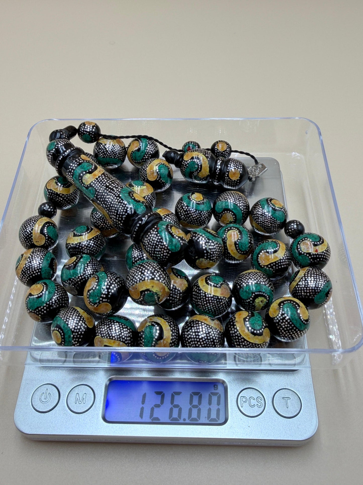 يسر بحر أحمر، مطعّم بالفضّة الخالصة عيار 925، ومزيّن بـ الكهرمان الطبيعي والملاكيت.
Red Sea Yusr, inlaid with 925 sterling silver, adorned with natural amber and malachite.