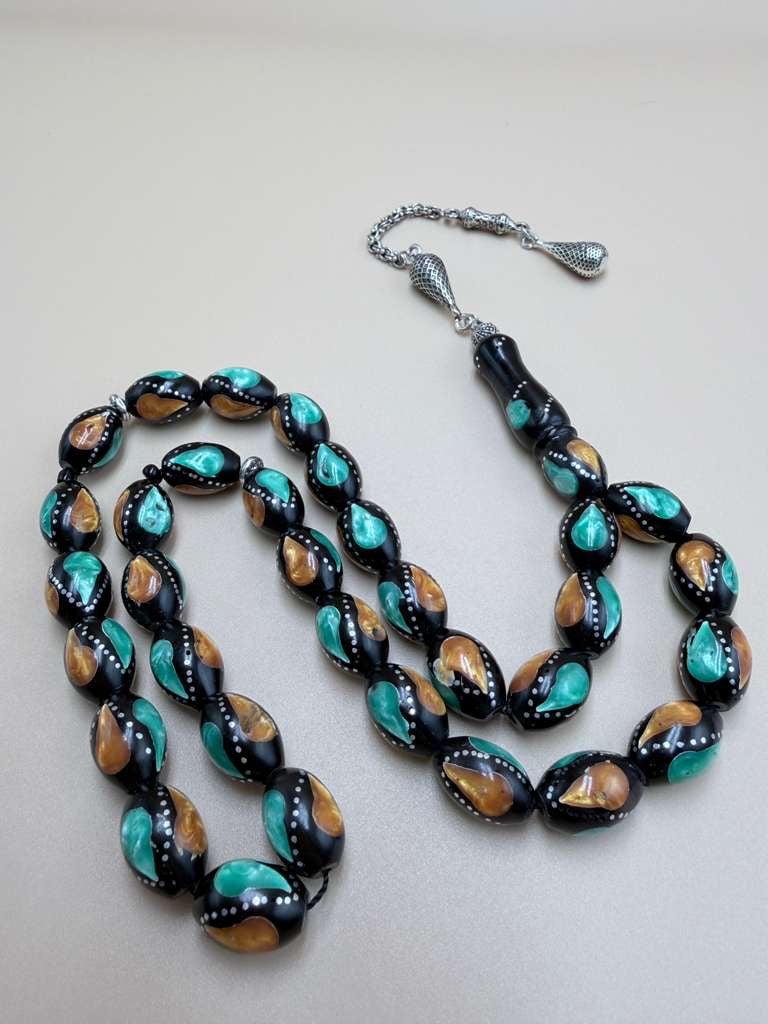 مسباح كوك، مطعّم بطحين الكهرمان وحجر المالاكيت والفضة. Kuka Wood Misbah, Inlaid with Amber Powder, Malachite Stone, and Silver.